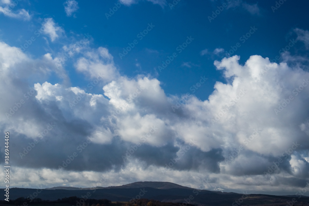 White-blue clouds in the sky above the rolling valley before the storm. White-blue clouds in the sky above the rolling valley before the storm.