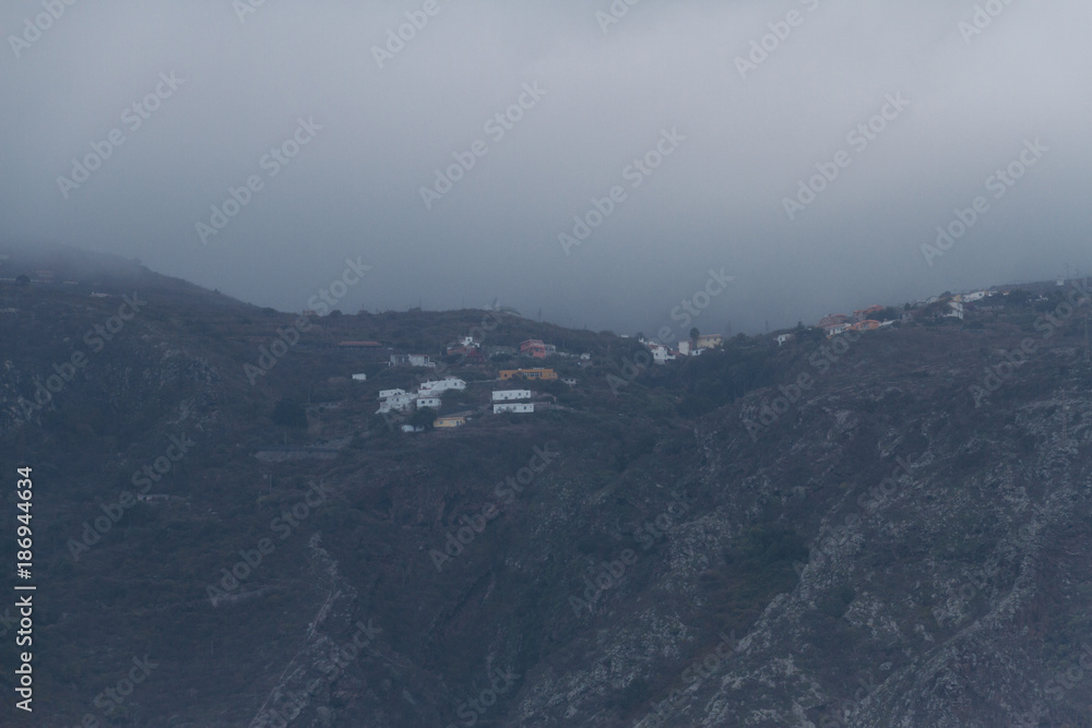 Village in hills covered in atmospheric fog and clouds