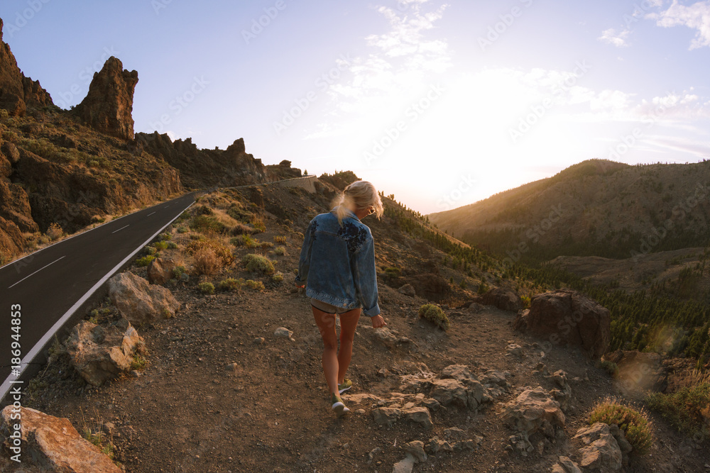 Fototapeta premium Girl in mini shorts and jeans jacket hiking and looking at sunset in desert nature