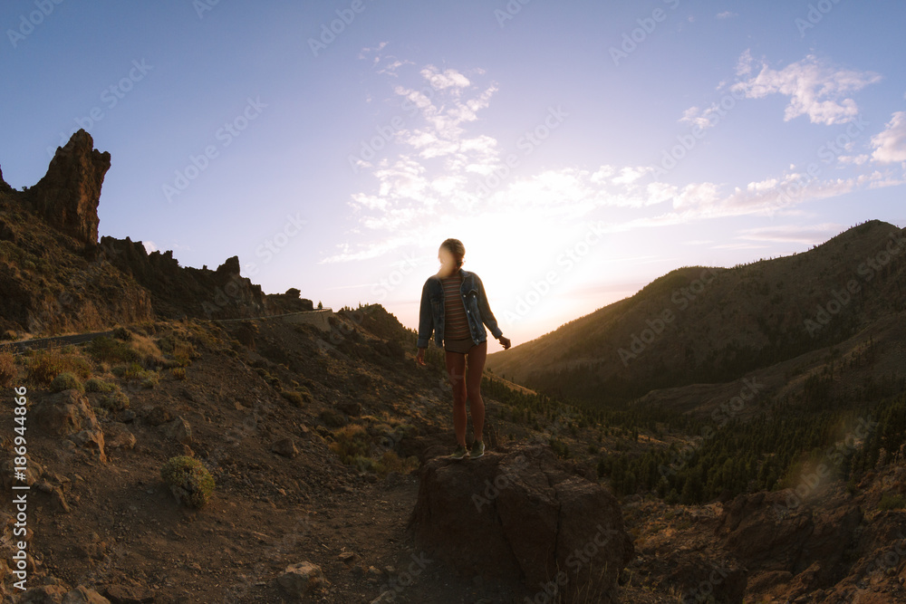 Fototapeta premium Girl in mini shorts and jeans jacket hiking and looking at sunset in desert nature