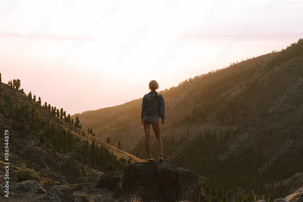 Girl in mini shorts and jeans jacket hiking and looking at sunset in desert nature