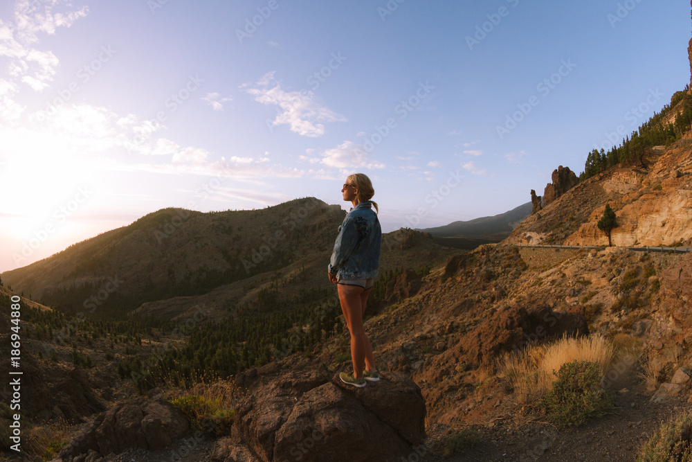 Girl in mini shorts and jeans jacket hiking and looking at sunset in desert nature