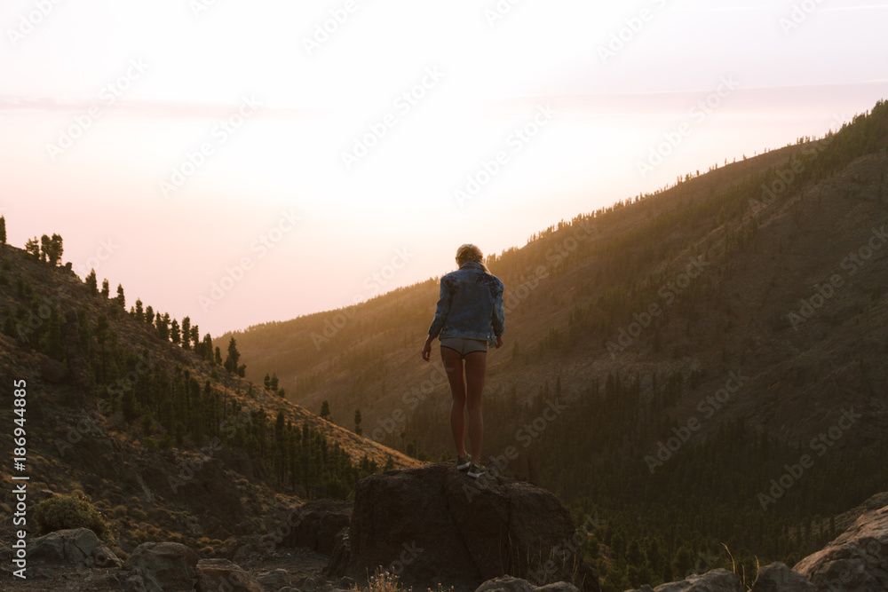 Girl in mini shorts and jeans jacket hiking and looking at sunset in desert nature