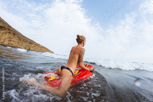 Young topless girl in thongs on pool float in ocean waves