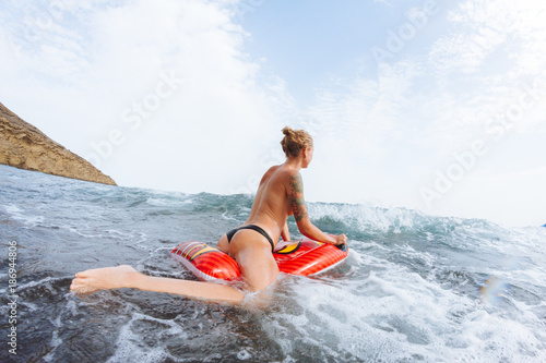 Young topless girl in thongs on pool float in ocean waves