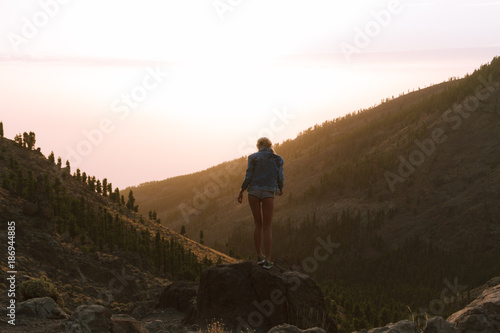 Girl in mini shorts and jeans jacket hiking and looking at sunset in desert nature