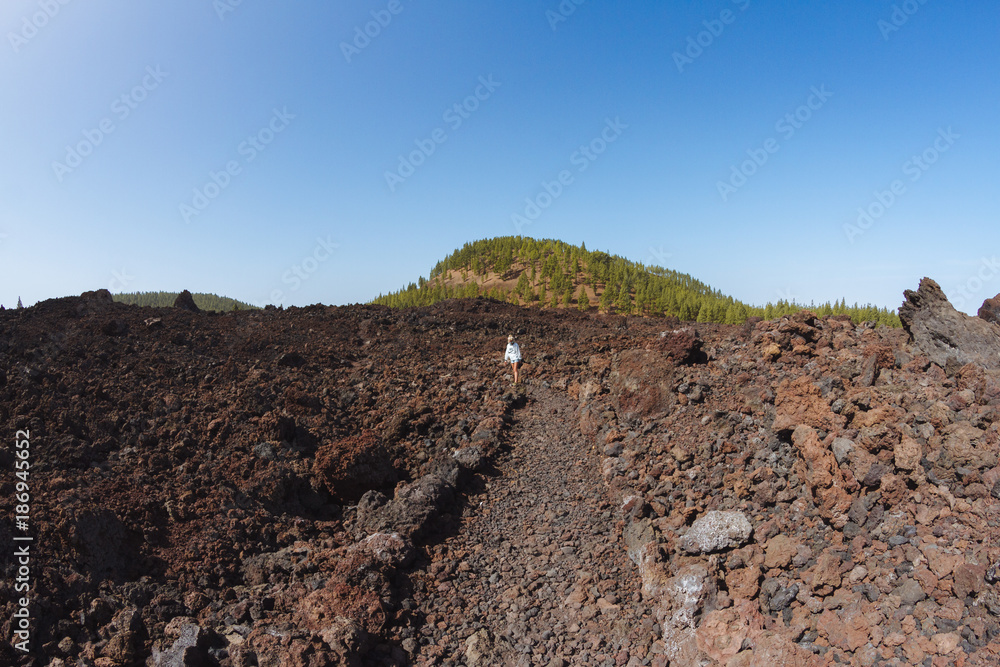 Girl walking in dark volcanic landscape with green trees