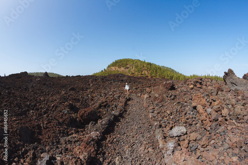 Girl walking in dark volcanic landscape with green trees