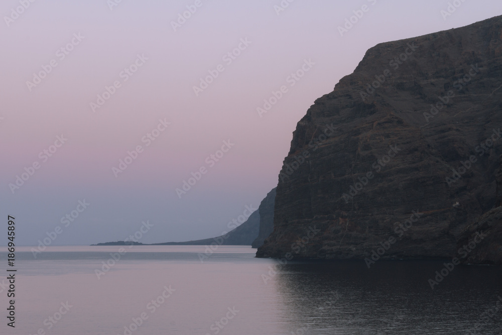 Calm ocean water and big cliffs in dusk before sunrise