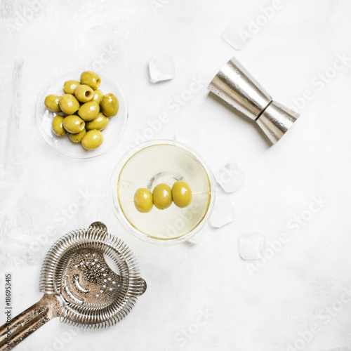 Fotografie Classic alcoholic cocktail with dry vermouth and green olives, bar tools, gray b