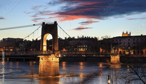 Illuminated Passerelle du College over the Rhone river in Lyon, France, during sunset.