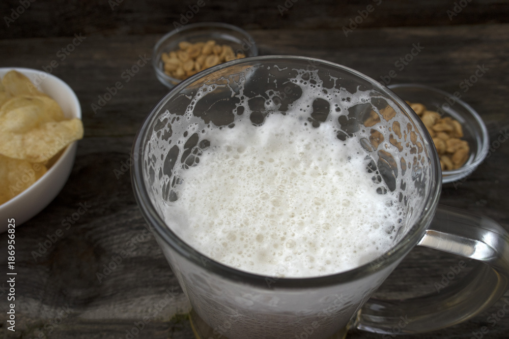 Mug with foam beer, chips and nuts on a wooden background.