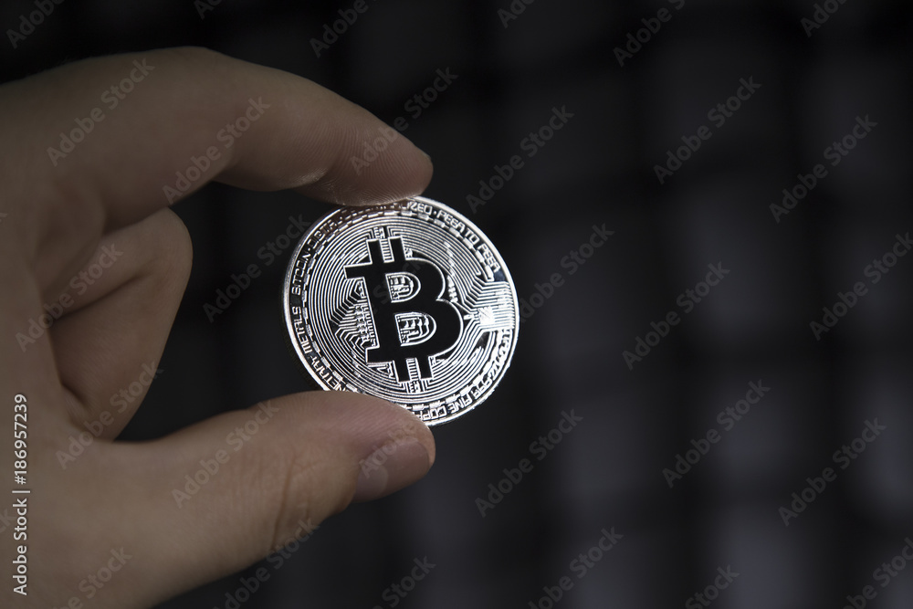 A man holding a silver bitcoin on a dark background. A man holding a silver bitcoin on a dark background.
