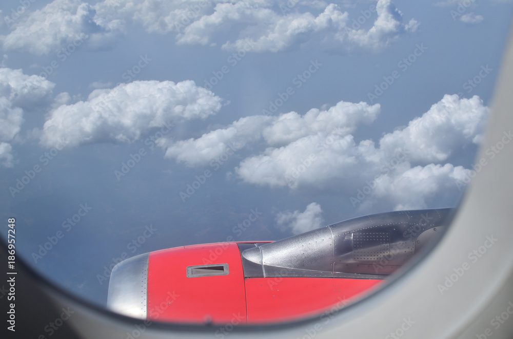 View through airplane window to its engine and clouds in distance during the flight