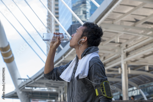 Asian sport man is drinking water from bottle after exercise 