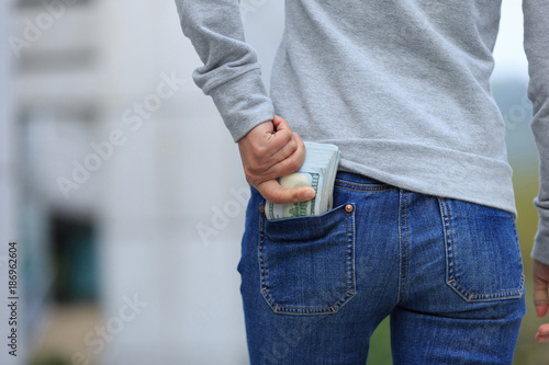 Female hand put money into pocket on blurred city background