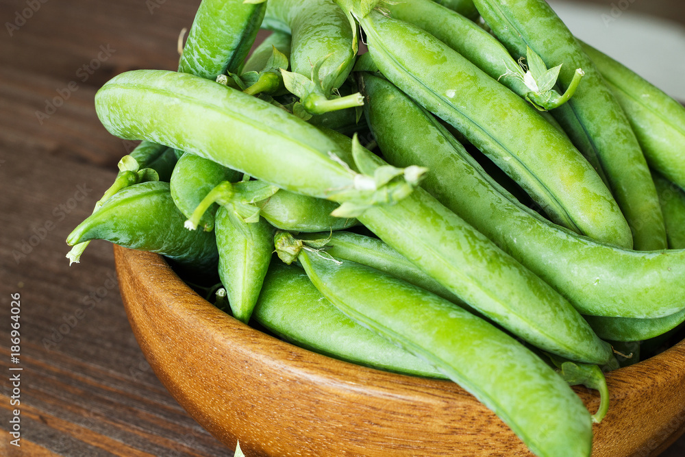 Pods of green peas in a wooden bowl. Pods of green peas in a wooden bowl.