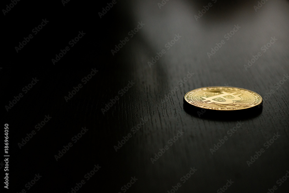 Golden bitcoin coin on the black wooden table. Close up (macro) with black background.
