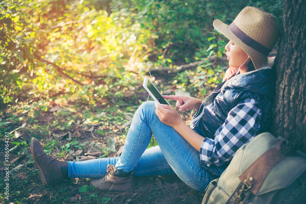 Woman hiker use digital tablet at mountain. Young woman traveller with backpack in a woods. Hiking at summertime. Woman hiker use digital tablet at mountain. Young woman traveller with backpack in a woods. Hiking at summertime.