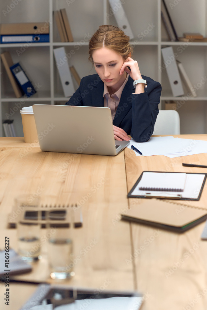 Pensive woman sitting at table and looking on laptop Pensive woman sitting at table and looking on laptop