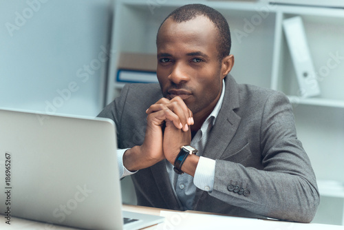 pensive african man sitting at table with laptop at office space