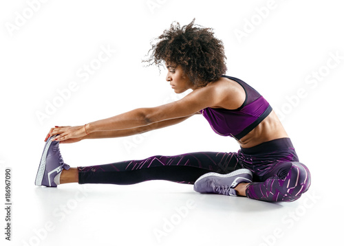 Sporty girl stretching her hamstrings. Photo of african girl doing exercising on white background. Sports © Romario Ien