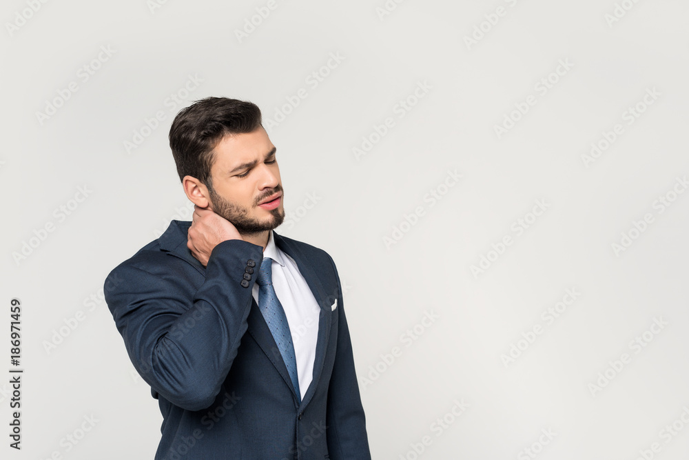 young businessman with closed eyes suffering from pain in neck isolated on grey young businessman with closed eyes suffering from pain in neck isolated on grey