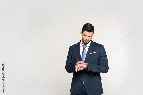 fashionable young businessman checking wristwatch isolated on grey