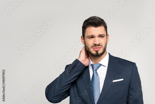 young businessman suffering from pain in neck and looking away isolated on grey