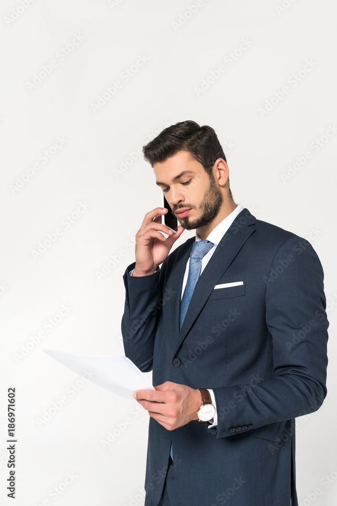 young businessman talking on smartphone and looking at paper isolated on grey young businessman talking on smartphone and looking at paper isolated on grey