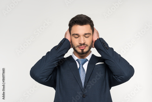 relaxed young businessman with closed eyes closing ears with hands isolated on grey