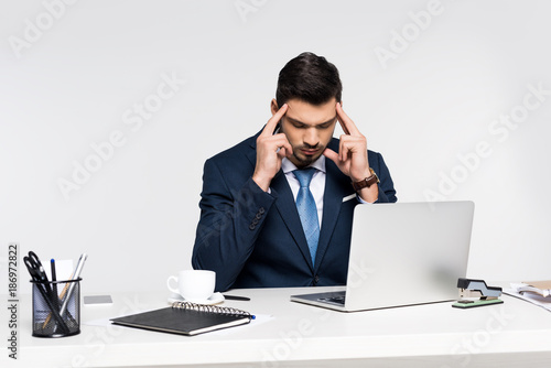 young businessman suffering from headache while using laptop at workplace