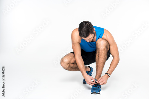 athletic young man lacing up sneakers before run on white