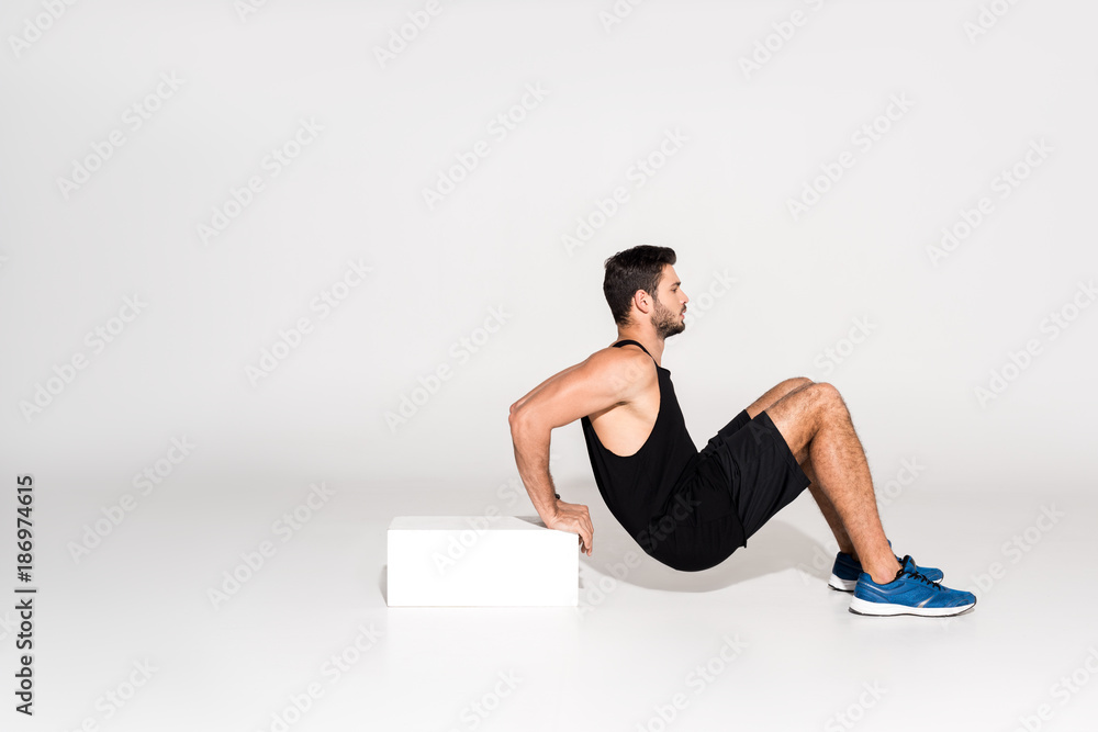 Fototapeta premium side view of young man doing reverse push ups with block