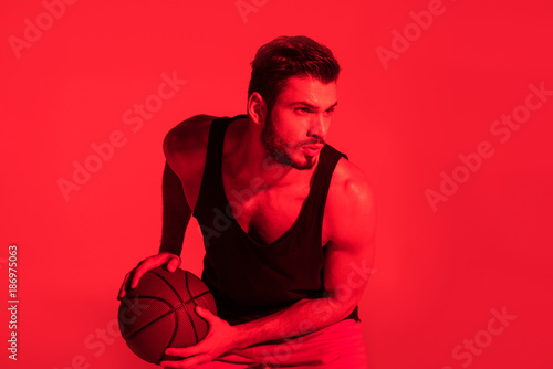 focused young sportsman playing basketball at contrast red light