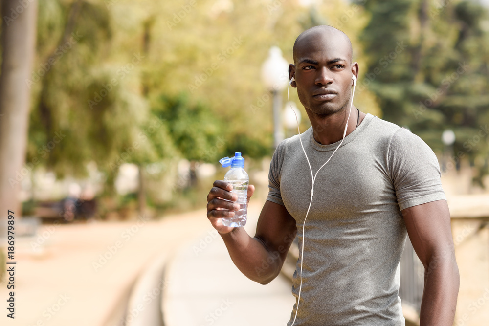 Young black man drinking water before running in urban background Young black man drinking water before running in urban background