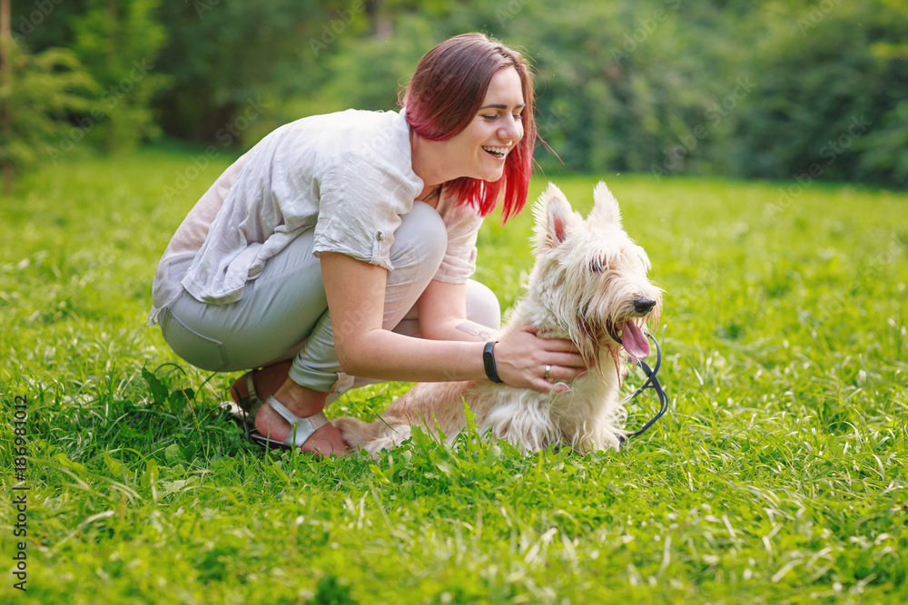 Smiling young woman in grey pants and t-shirt with dog in park Smiling young woman in grey pants and t-shirt with dog in park