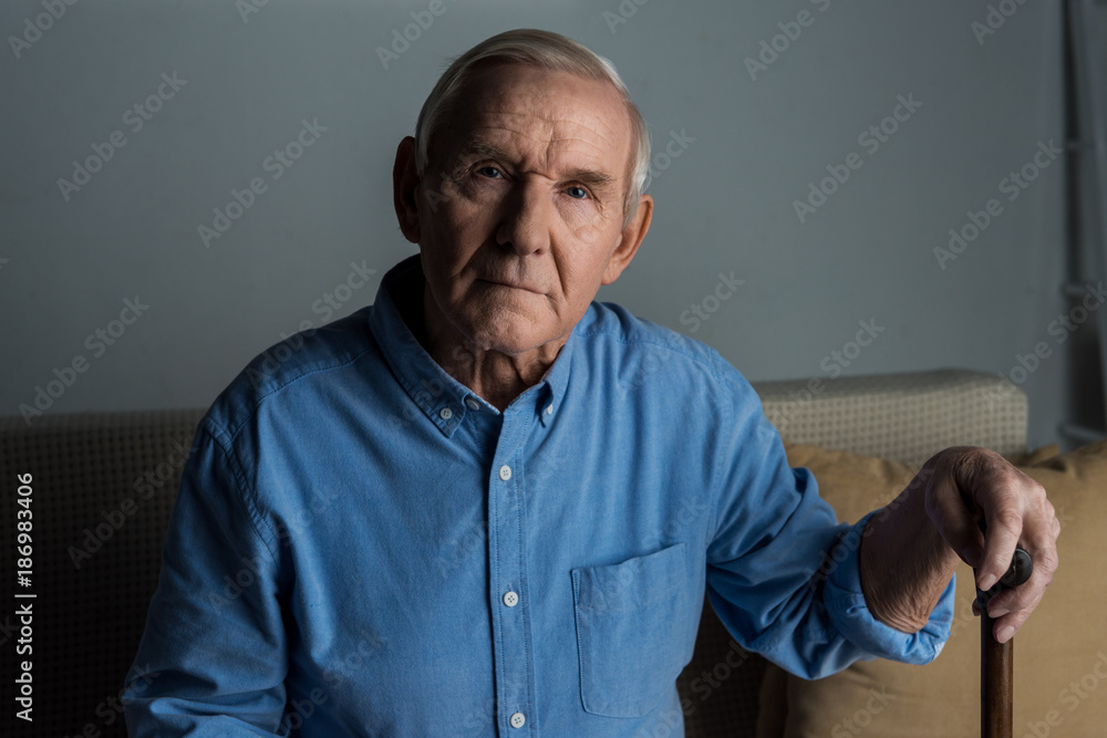 Fototapeta premium Senior confident man leans on a cane while sitting on sofa