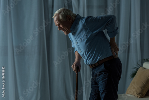 Senior man suffering from back pain leans on a cane