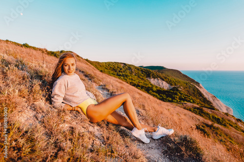Attractive woman relaxing in nature at warm sunset. Fitness girl in the mountains