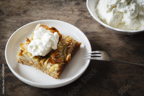 Piece of whole meal apple pie with sliced almonds and whipped cream