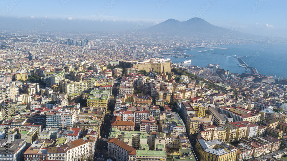 Fototapeta premium Aerial view of Naples from the Vomero district. You can see Castel Sant'elmo in the foreground while in the background the city's port, the Vesuvius and the Ovo castle. There are houses and buildings.