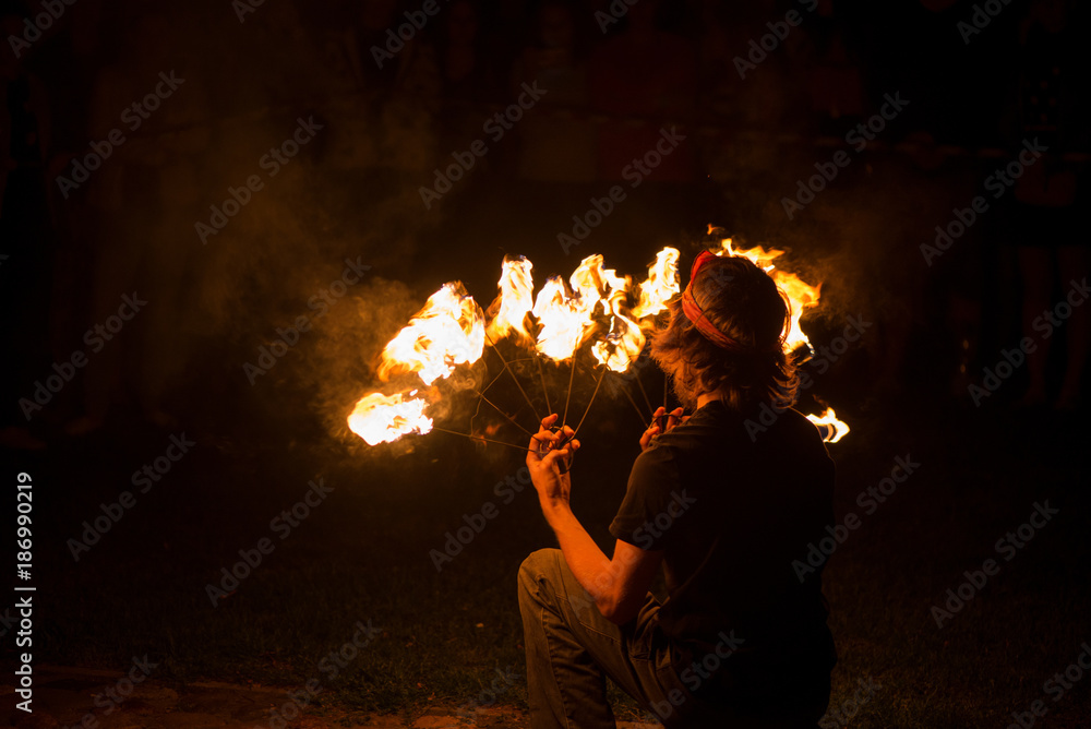 Young male performing fire juggling in front of excited crowd. Fire show and performance at night. 