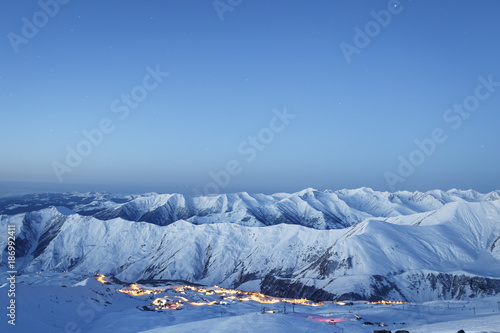 Snow-covered mountains in the early morning. In the valley illuminated ski resort Gudauri. Georgia. Caucasus.