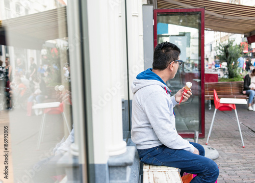 Man with icecream sitting on bench at store window. Deventer, Overijssel, Netherlands.