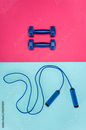 Sports dumbbells and skipping rope isolated on pink and blue