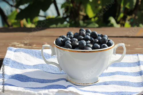 Closeup on a tasty ripe freshly picked blueberries in a white vintage ceramic bowl. Selective focus, free text space. Fruits harvested in summer. Healthy fruit,blurred background.