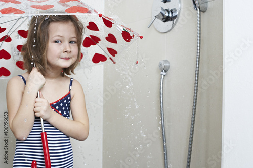 Portrait of smiling little girl taking shower with umbrella photo