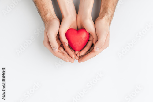 top view of hands of elder person and smaller one holding red heart isolated on white background