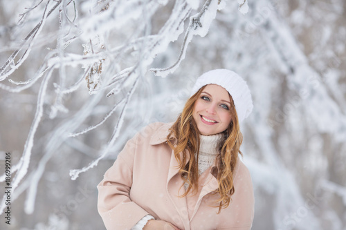 Portrait of smiling young pretty woman in a beige coat touches a hat in a winter